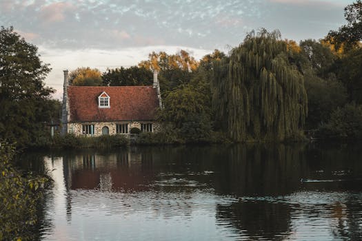 A picturesque lakeside cottage surrounded by lush trees, reflecting in calm waters.